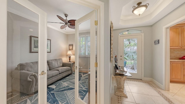 entryway featuring light tile patterned floors, baseboards, a tray ceiling, ceiling fan, and ornamental molding