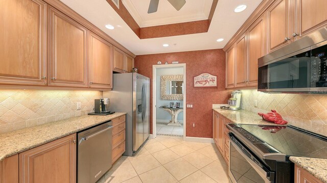 kitchen featuring crown molding, light stone countertops, a tray ceiling, light tile patterned floors, and stainless steel appliances