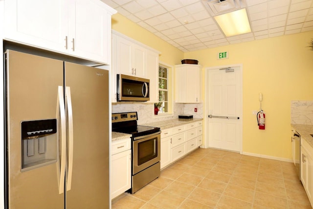 kitchen featuring light stone counters, appliances with stainless steel finishes, white cabinets, light tile patterned floors, and decorative backsplash