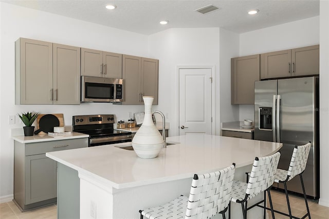 kitchen featuring visible vents, gray cabinetry, appliances with stainless steel finishes, a breakfast bar area, and light countertops