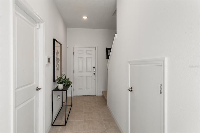 corridor featuring baseboards, a textured ceiling, and light tile patterned flooring