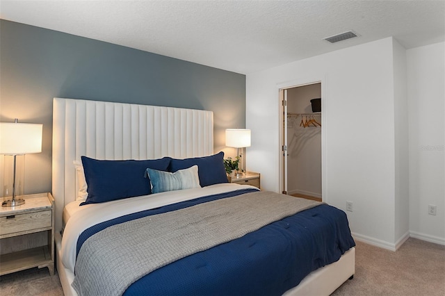 carpeted bedroom with a spacious closet, visible vents, baseboards, a closet, and a textured ceiling