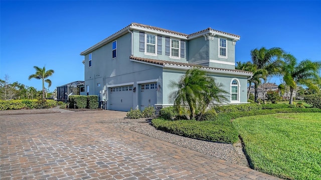 mediterranean / spanish house featuring decorative driveway, a tiled roof, an attached garage, and stucco siding