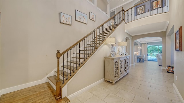 stairs featuring arched walkways, a high ceiling, baseboards, and ornamental molding