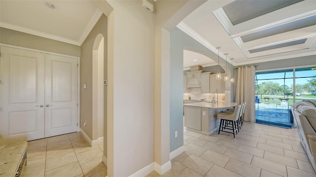 interior space featuring a sink, arched walkways, crown molding, light tile patterned floors, and baseboards