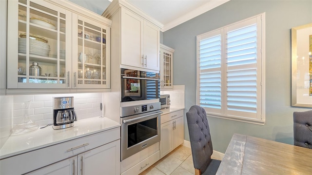 kitchen with decorative backsplash, light countertops, light tile patterned flooring, and glass insert cabinets