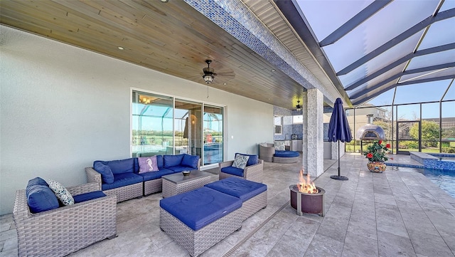 view of patio / terrace featuring a lanai, a pool with connected hot tub, an outdoor living space with a fire pit, and a ceiling fan