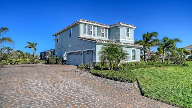 mediterranean / spanish home featuring decorative driveway, a garage, stucco siding, and a tiled roof