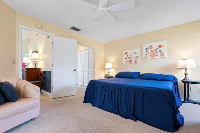 carpeted bedroom featuring a closet, visible vents, a textured ceiling, and a ceiling fan