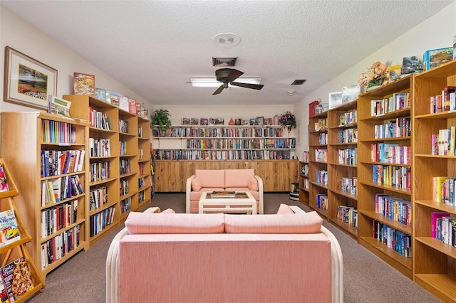 sitting room featuring bookshelves, visible vents, a textured ceiling, and carpet floors