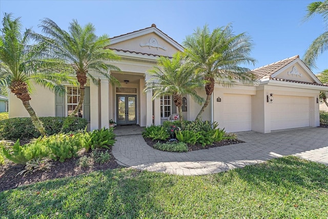 view of front of property featuring decorative driveway, an attached garage, french doors, and stucco siding