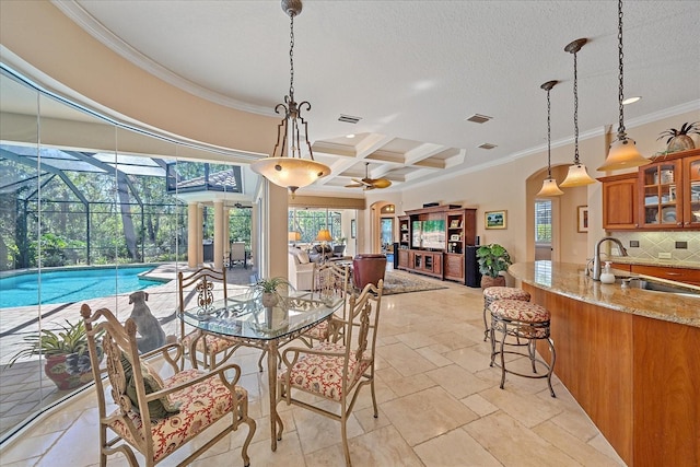 dining space with stone tile floors, coffered ceiling, beam ceiling, a sunroom, and crown molding