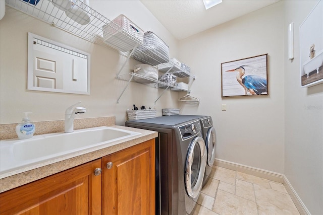 laundry area featuring a sink, stone tile floors, cabinet space, separate washer and dryer, and baseboards