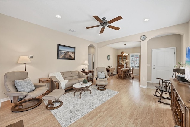 living area featuring ceiling fan with notable chandelier, visible vents, light wood-type flooring, and arched walkways