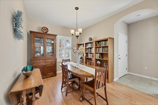 dining room with baseboards, arched walkways, light wood-style flooring, and a chandelier