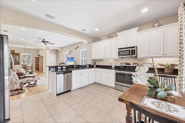 kitchen featuring visible vents, a peninsula, arched walkways, stainless steel appliances, and decorative backsplash