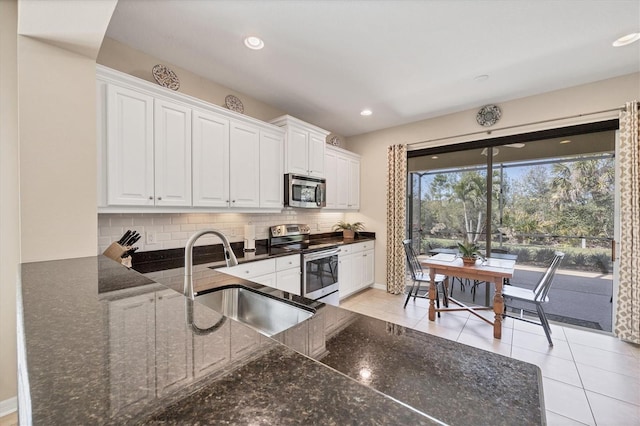 kitchen with dark stone countertops, a sink, decorative backsplash, stainless steel appliances, and white cabinets