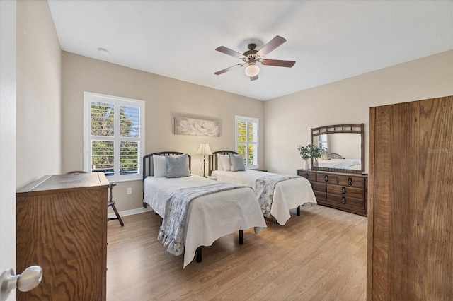 bedroom featuring light wood finished floors, multiple windows, baseboards, and ceiling fan