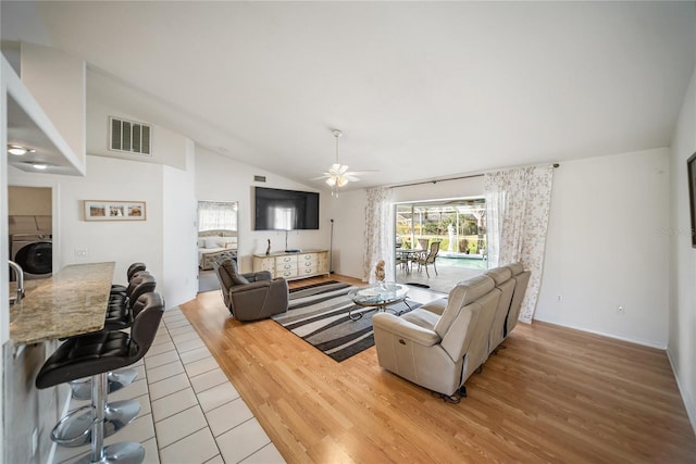 living room with visible vents, lofted ceiling, light wood-style flooring, washer / dryer, and a ceiling fan