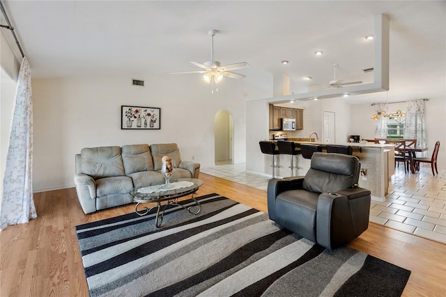 living room featuring light wood-type flooring, visible vents, arched walkways, and ceiling fan with notable chandelier