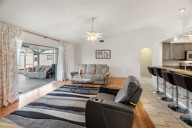 living area with visible vents, a ceiling fan, arched walkways, light wood finished floors, and lofted ceiling