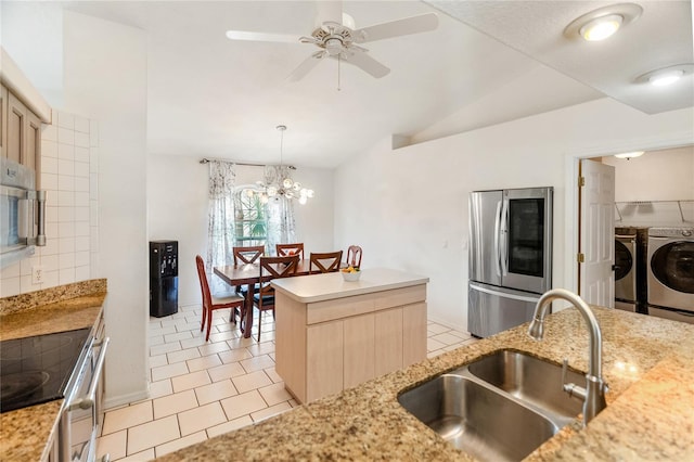 kitchen featuring light tile patterned floors, washing machine and clothes dryer, a sink, stainless steel appliances, and vaulted ceiling