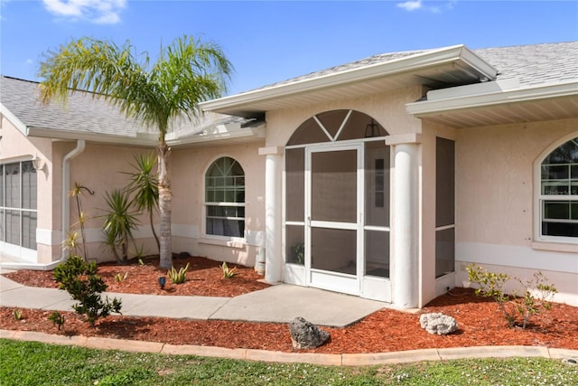 view of exterior entry featuring roof with shingles and stucco siding