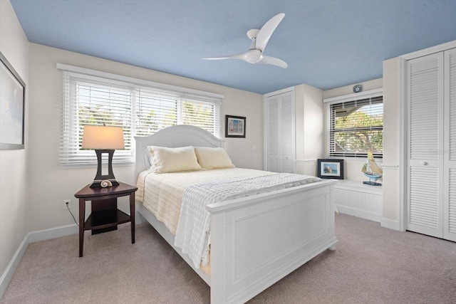 bedroom with baseboards, multiple closets, light colored carpet, and ceiling fan