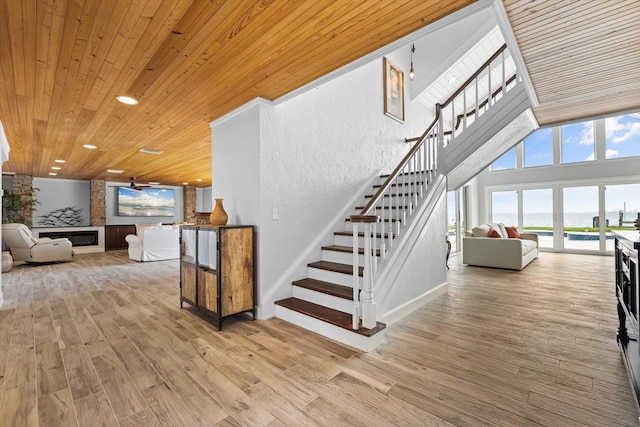 stairway featuring wood finished floors, recessed lighting, a large fireplace, wooden ceiling, and a towering ceiling