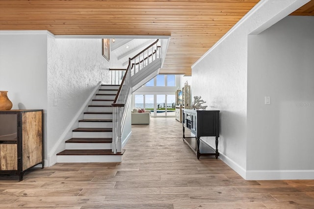 stairs with wood finished floors, wooden ceiling, crown molding, and a textured wall