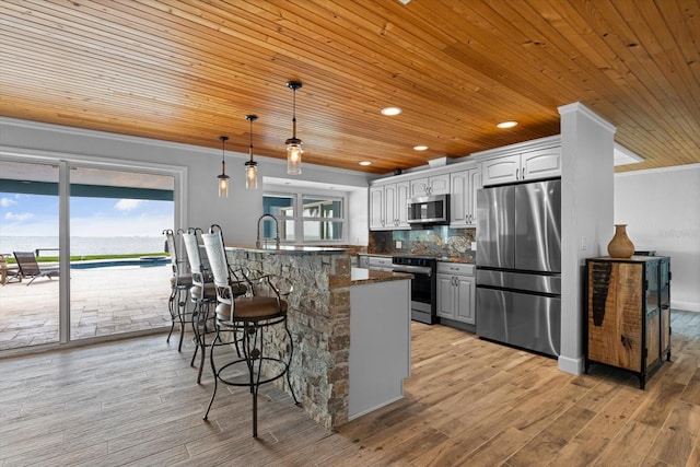 kitchen with a breakfast bar area, stainless steel appliances, light wood-style floors, crown molding, and tasteful backsplash