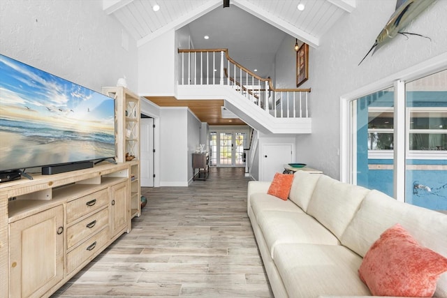 living room featuring stairway, beam ceiling, light wood-style floors, a textured wall, and high vaulted ceiling