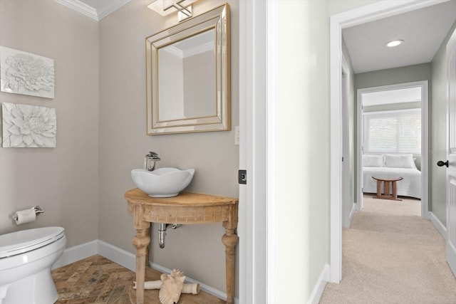 half bath featuring toilet, crown molding, baseboards, and a sink