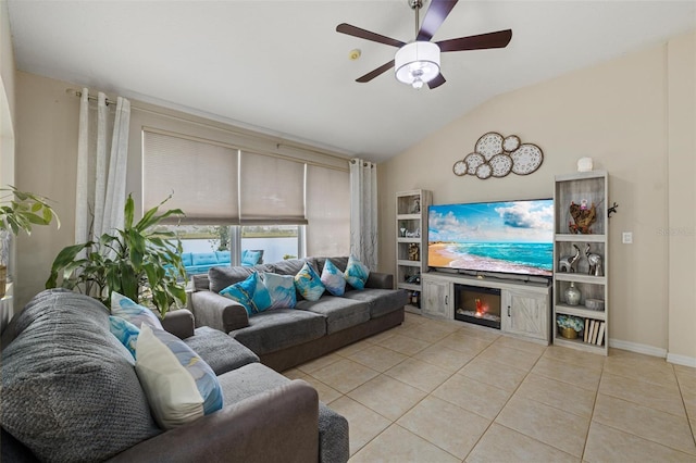 living room with light tile patterned floors, a ceiling fan, baseboards, vaulted ceiling, and a glass covered fireplace