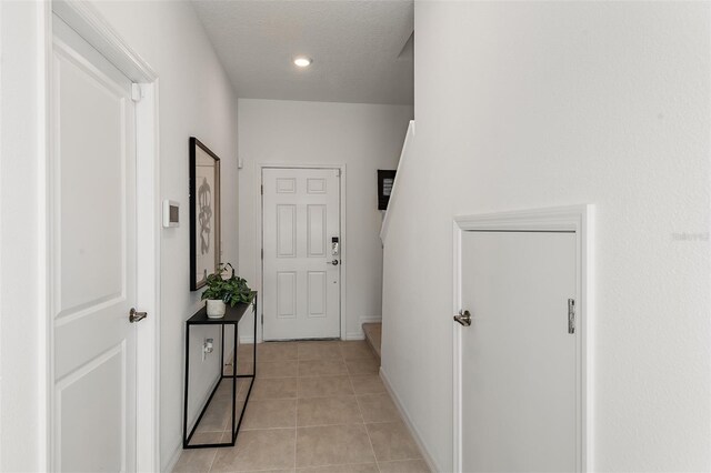 hall featuring light tile patterned floors, a textured ceiling, and baseboards