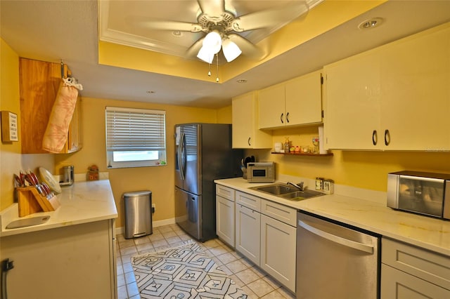 kitchen with crown molding, a tray ceiling, appliances with stainless steel finishes, light tile patterned flooring, and a sink