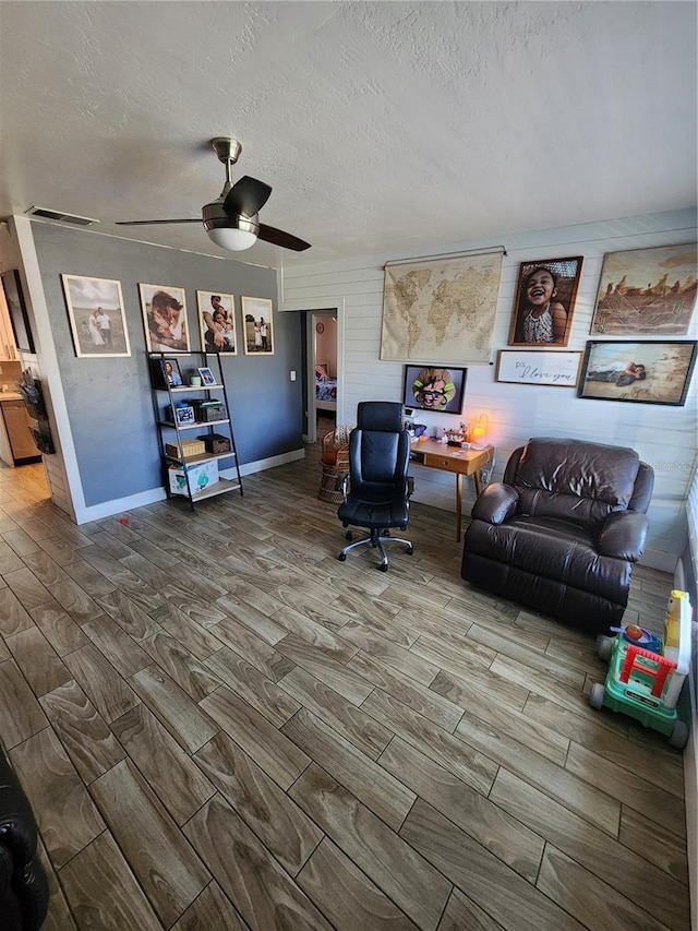 living room with a ceiling fan, wood finished floors, visible vents, and a textured ceiling