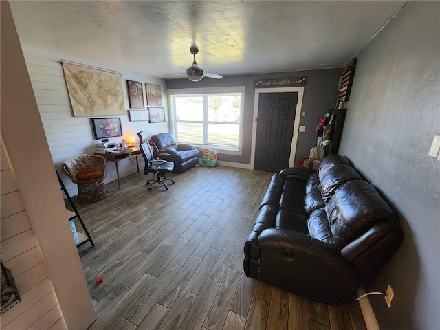 living room with a textured ceiling, wood finished floors, a textured wall, and ceiling fan