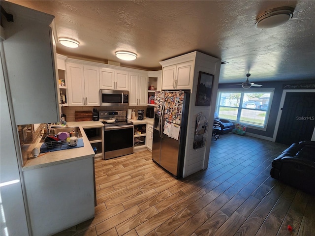 kitchen featuring light countertops, light wood-style flooring, stainless steel appliances, white cabinetry, and open shelves