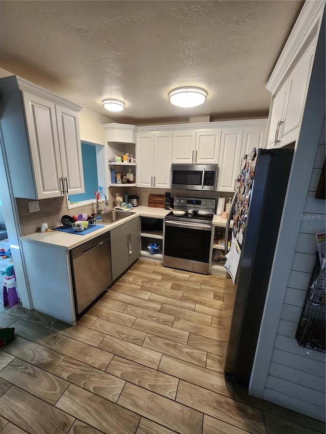 kitchen featuring wood tiled floor, open shelves, a sink, stainless steel appliances, and white cabinets