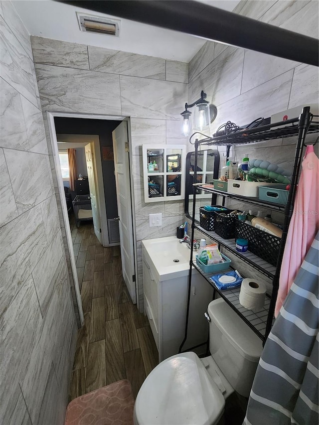 bathroom featuring vanity, wood finished floors, visible vents, tile walls, and toilet