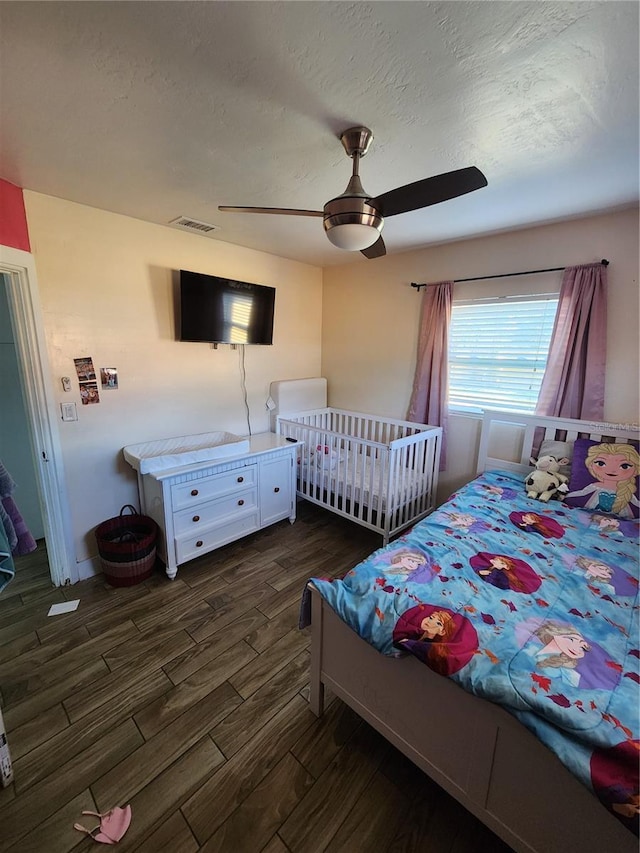 bedroom with visible vents, dark wood-type flooring, a ceiling fan, and a textured ceiling