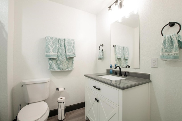 half bathroom featuring baseboards, toilet, wood finished floors, and vanity