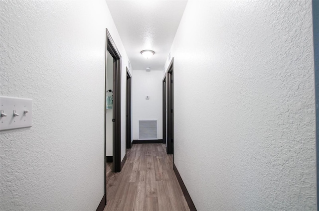 hallway with visible vents, baseboards, wood finished floors, and a textured wall