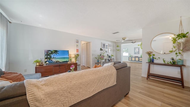 living room featuring light wood finished floors, visible vents, a textured ceiling, and ceiling fan