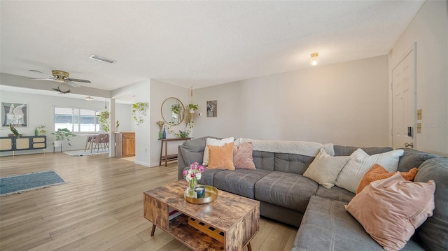 living area featuring ceiling fan, light wood-style flooring, visible vents, and a textured ceiling