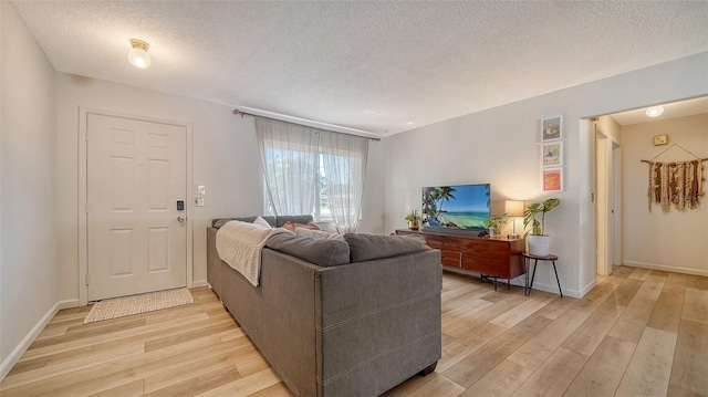 living room featuring light wood finished floors, a textured ceiling, and baseboards