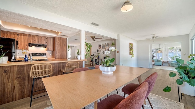 dining space with a ceiling fan, light wood-style floors, visible vents, and a textured ceiling