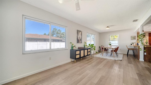 dining room with baseboards, visible vents, light wood finished floors, ceiling fan, and a textured ceiling