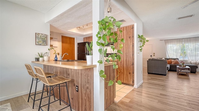 bar with baseboards, light wood-style flooring, stainless steel refrigerator, a textured ceiling, and a sink